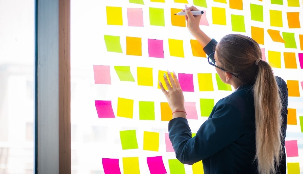 A female knowledge worker in front of a whiteboard with a large number of sticky notes.