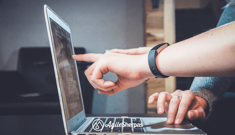 A picture showing a laptop and the hands of two men. One is scrolling on the touch pad, the other - pointing at the value stream map on the screen. 