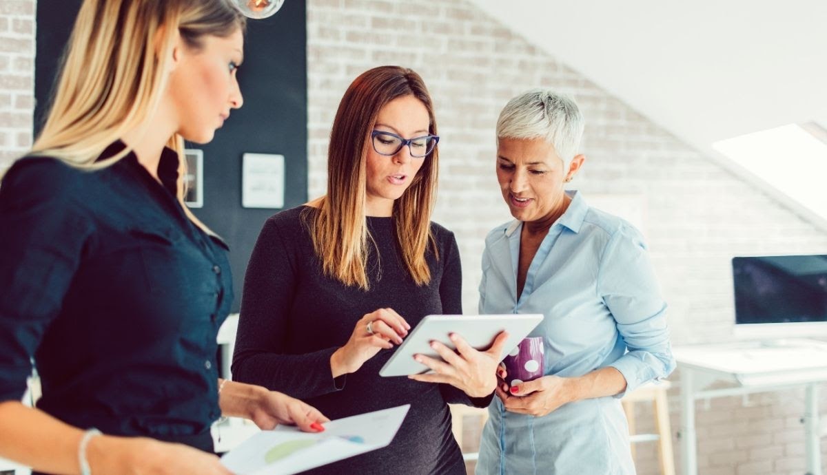 Three female marketers looking at a tablet and having a discussion.